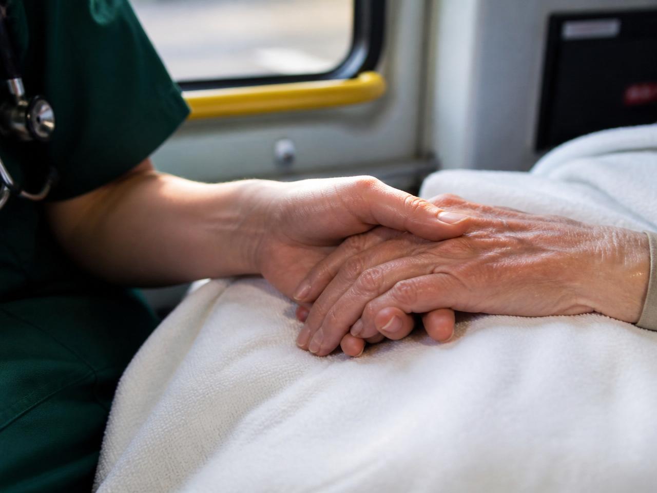 Caregiver's hand holding an elderly patient's hand inside a medical transport van